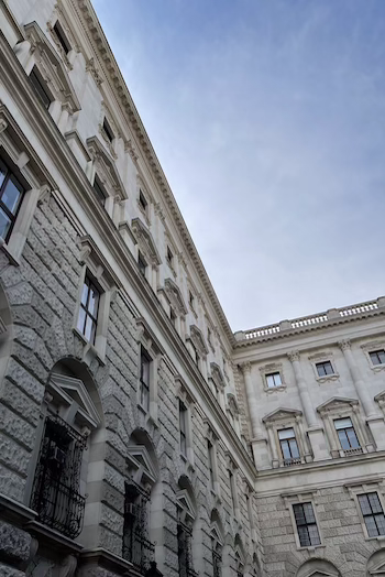You can the see one of the buildings from the Hofburg in Vienna. The photo is shot from below and you can see the blue sky. The building has a lot of windows and a lavish facade.