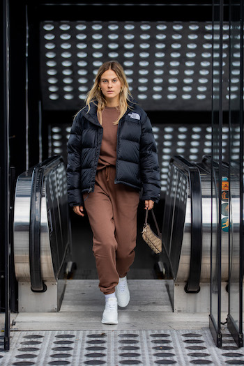 @alexawinter is standing in front of the escalator and comes running towards the photographer. She wears a dark brown loungewear suit in combination with a black puffer jacket from The North Face and the CPH40 in vitello white.