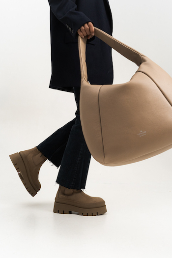 On this picture you can see the lower body part of a person who is carrying the CPH Bag 12 in nappa cappuccino in his right hand. The person is wearing matching boots. 