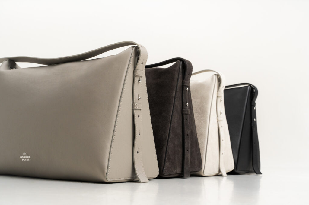 This picture shows the CPH Bag 8 in four different colors. The bags are placed right next to each other. The color of the first bag on the left side is stone, the next one is off black, then almond and the bag on the right is black. 