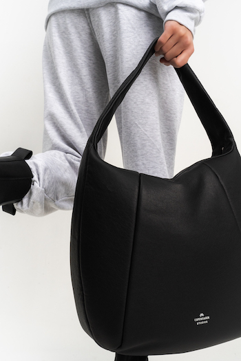 This picture shows the legs of a person who is wearing sweatpants, holding the CPH Bag 12 in nappa black. The bag has a short leather strap and the shape is round.