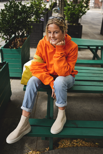 Josephin Jein's ideal spot to enjoy the beautiful Copenhagen summer is the street food market Broens Gadekøkken. She is sitting there and wearing a orange sweatshirt, a light blue jeans and CPH113 in morbidone stone.