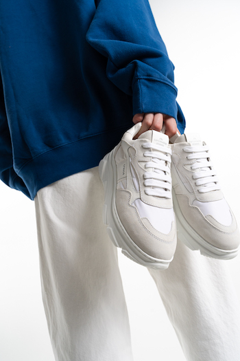 CPh51 material mix white. Model is holding a white sneaker in her hand. She is wearing a white jeans with a blue sweater.