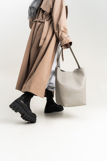 cph686 vitello black. The model is wearing black boots with a plateau sole and is holding a CPH Bag in her hand. She styled the look with a trench coat and a jogger pants.
