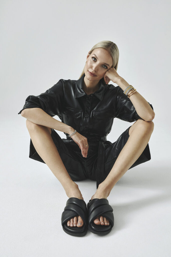Picture from the Copenhagen Studios Editorial Shooting: The Retro Super Future with Leonie Hanne, Lorena Rae and Najiyah Imani. On the picture you can see Leonie Hanne sitting while she is looking at the camera. She wears a black leather jumpsuit and the CPH726 kappa black sandals.