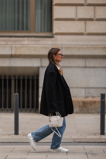 @annawntr on the streets of Hamburg city. She wears a black oversized Blazer, a cropped white blouse, denim jeans and her CPH Hamburg 2 vitello white.