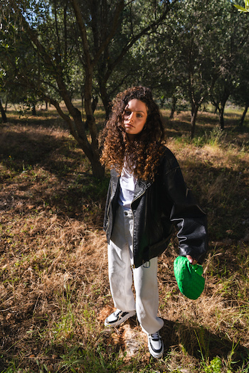A picture from the High Summer Campaign from Copenhagen Studios with the winner go our challenge at THOC. The model is standing and wearing a leather jacket and white jeans with the new CPH332 Sneakers in black/white.