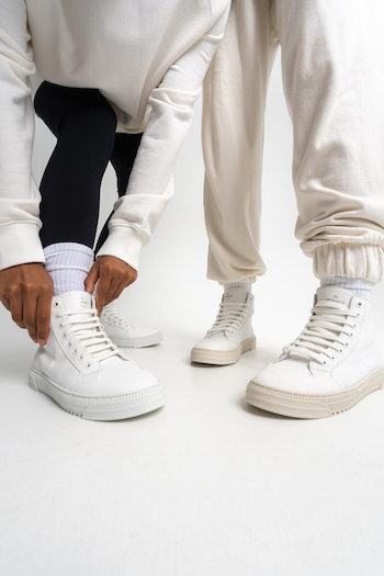 Two people wearing a high top sneaker. A classic model is the high-top canvas sneaker with a classic trainer silhouette. The shoe is made out of recycled material. The rubber sole with serrated tread and logo is inspired by the 80s and is perfect for relaxed everyday looks. 