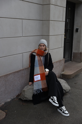 @tineandreaa sitting in the "Botanical Garden" in Oslo and wearing her CPH SHAWL 2 wool mix blue/orange. She combined it with an black wool trenchcoat, a black denim, an grey sweater, a grey wool beanie and the CPH332 leather mix black/white.