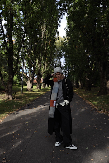 @tineandreaa standing in the "Botanical Garden" in Oslo and wearing her CPH SHAWL 2 wool mix blue/orange. She combined it with an black wool trenchcoat, a black denim, an grey sweater, a grey wool beanie and the CPH332 leather mix black/white.