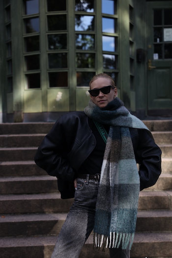 @tineandreaa standing in the "Botanical Garden" in Oslo and wearing her CPH SHAWL 2 wool mix green. She combined it with a black bomber jacket, grey denim and black sunglasses.