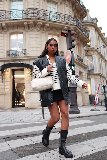 Photo from Paris. Women crosses the street. She wears a stripped jumper, leather vest, black shorts and mid high Copenhagen Studios boots.