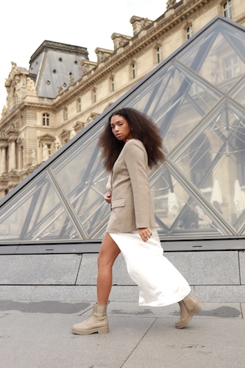 Women in Paris. She wears a white skirt, an oversized blazer and beige Copenhagen Studios boots.