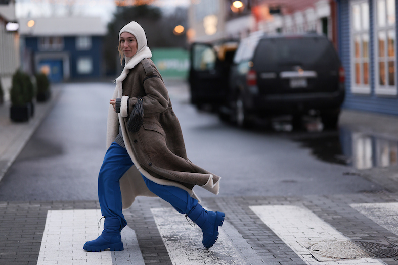 The fashion influencer Sonia Lyson is wearing a moon boot from our new collection in royal blue. She styled it with a blue pants and a long leather coat. She is crossing a street on Iceland.