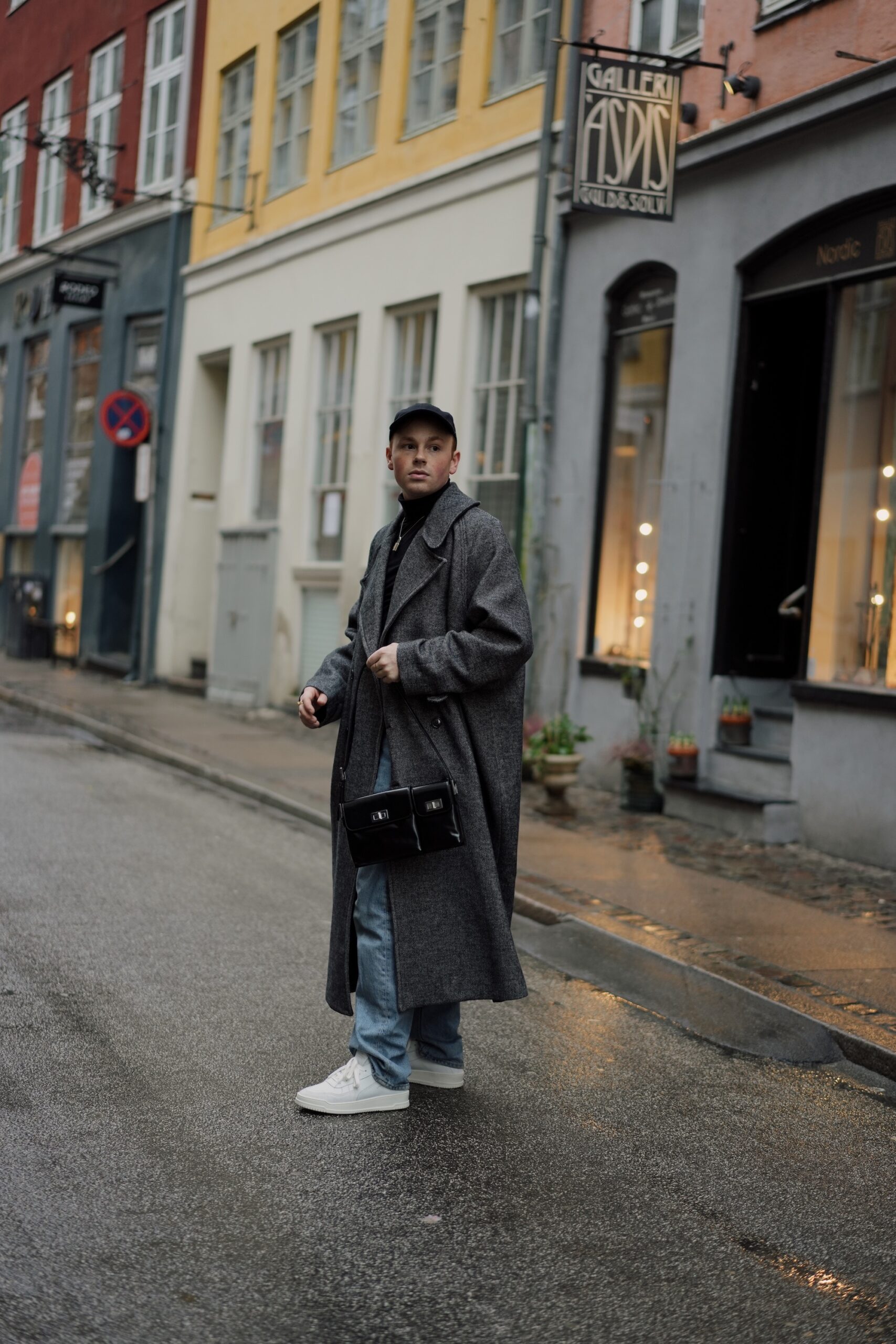 The young male influencer Erik Scholz is standing on the streets of copenhagen wearing our latest spring sneaker. The CPH161 leather mix white combined with an oversized grey wool coat and denim trousers. 