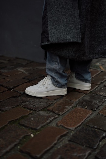 The young male influencer Erik Scholz is standing on the streets of copenhagen wearing our latest spring sneaker. The CPH161 leather mix white combined with an oversized grey wool coat and denim trousers. 