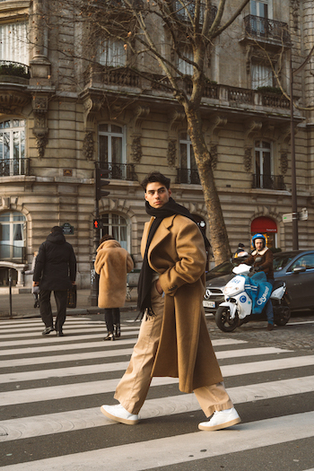 the young creator Jacob Rott walking a crosswalk in Paris, wearing beige trousers and a beige over-sized coat. He finished off his outfit wearing our CPH156 material mix white