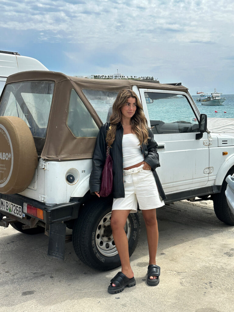 @brunabaer a young female creator form the Netherlands is wearing our CPH836 in vitello black and combined it with an oversized leather jacket. She is standing in front of an old white pick-up next to seaside.