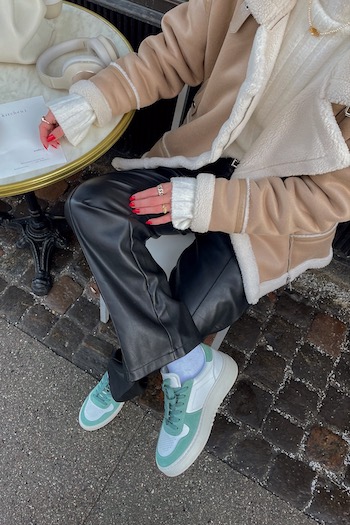 The danish creator Amanda sand sitting in a cafe, eating a lemon poppyseed cake and wearing our cph77 leather mix white/sage sneaker.