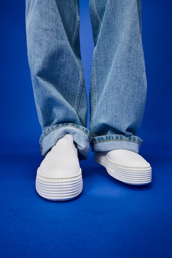 Our white sneaker CPH204 leather milk worn by a model wearing denims, standing on a blue backdrop.