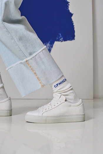 A model wearing denims standing a white backdrop. She is wearing our CPH4 soft vitello white and some of our latest socks.