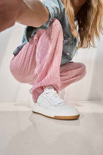 A female model wearing a jeans blouse and striped pink jeans, wearing the CPH213 soft vitello white. She is taking a selfie, putting the shoe in focus.