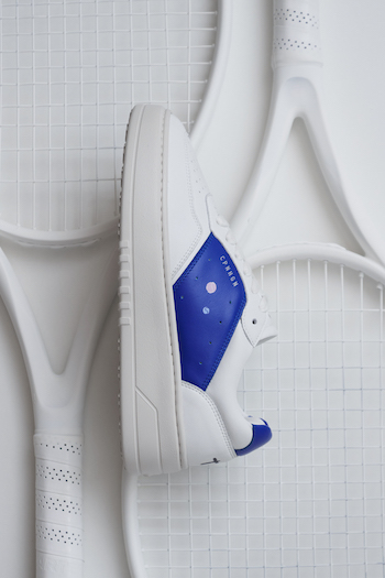 The CPH NEW YORK leather white/pink/blue is in focus & laying on a racket.