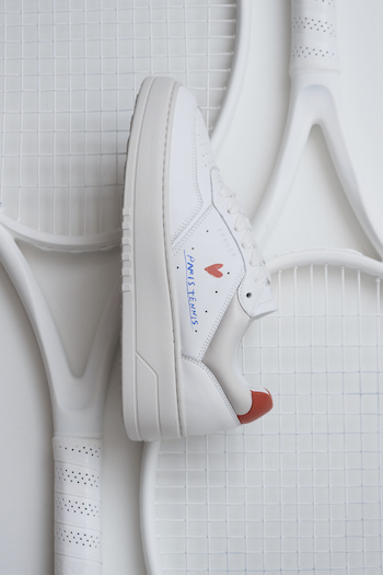 The CPH PARIS leather white/orange is in focus & laying on a racket.