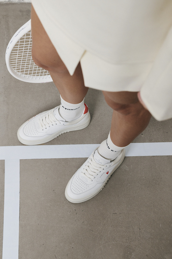 You can see a model posing in the CPH PARIS with a racket and wearing a tennis skirt & beige sweater.