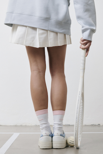 You can see a model posing in the CPH MELBOURNE with a racket and wearing a tennis skirt & gray sweater.